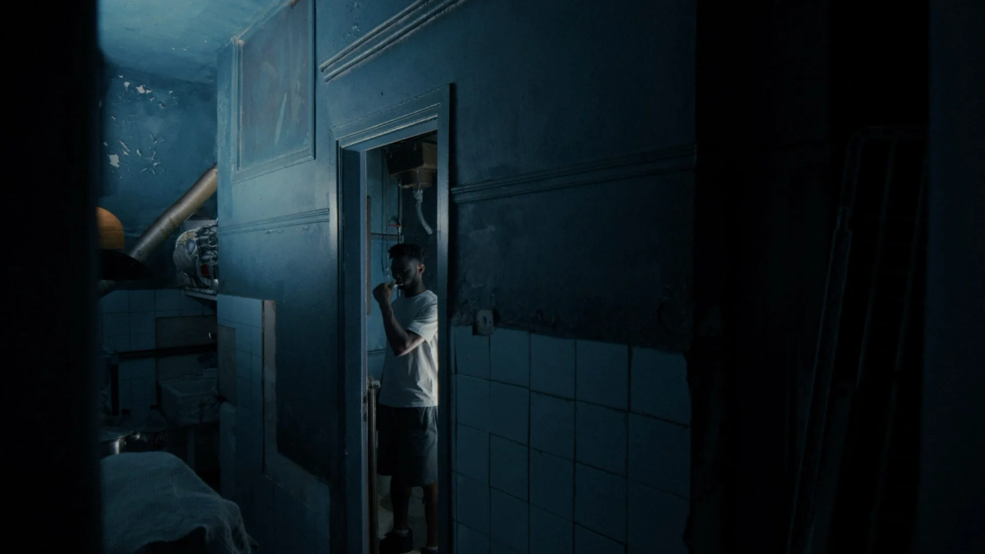 Cinematic still from a narrative short — figure in a doorway, blue-toned interior